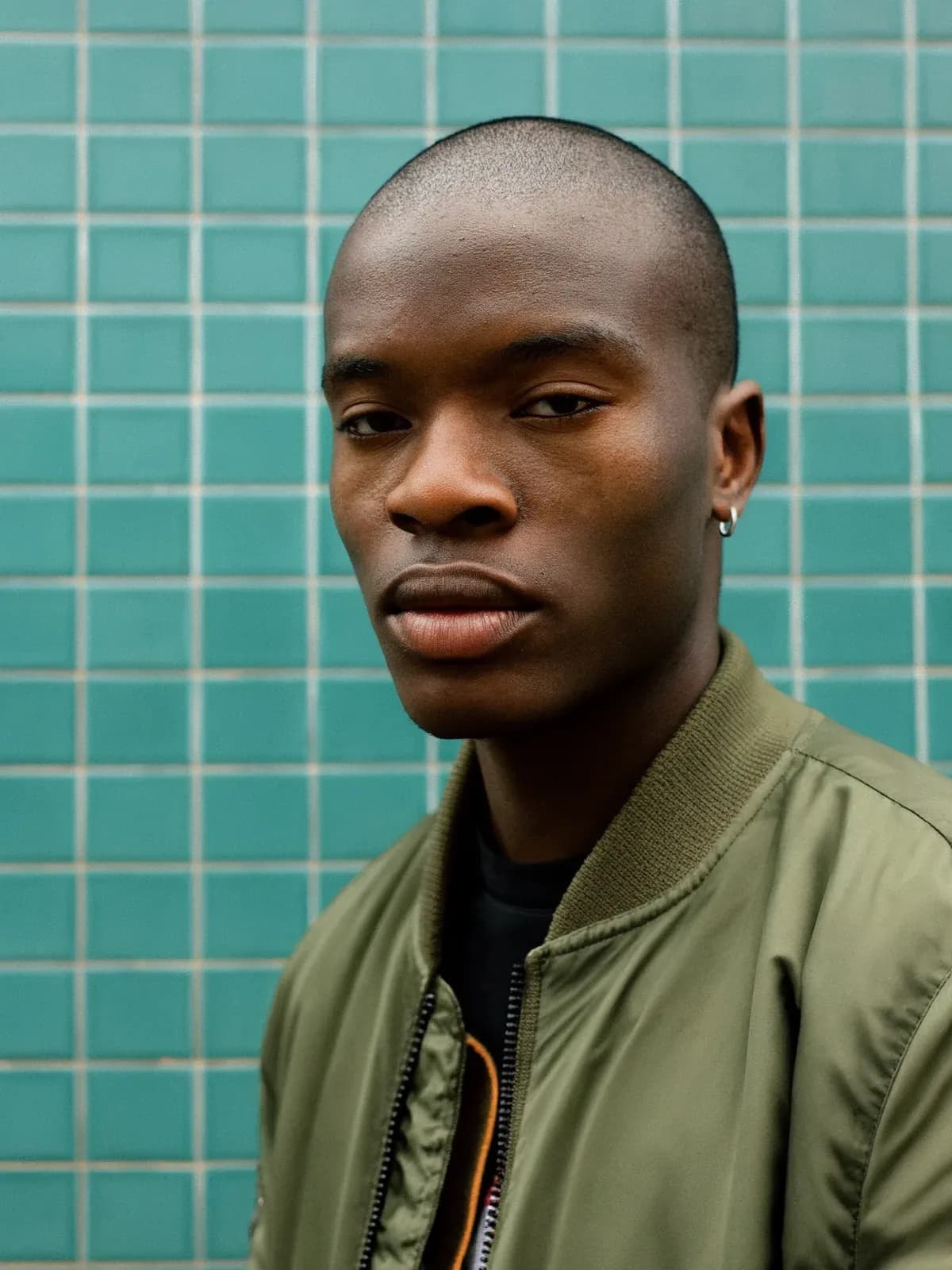 Portrait of a young man in an olive bomber against teal tiles