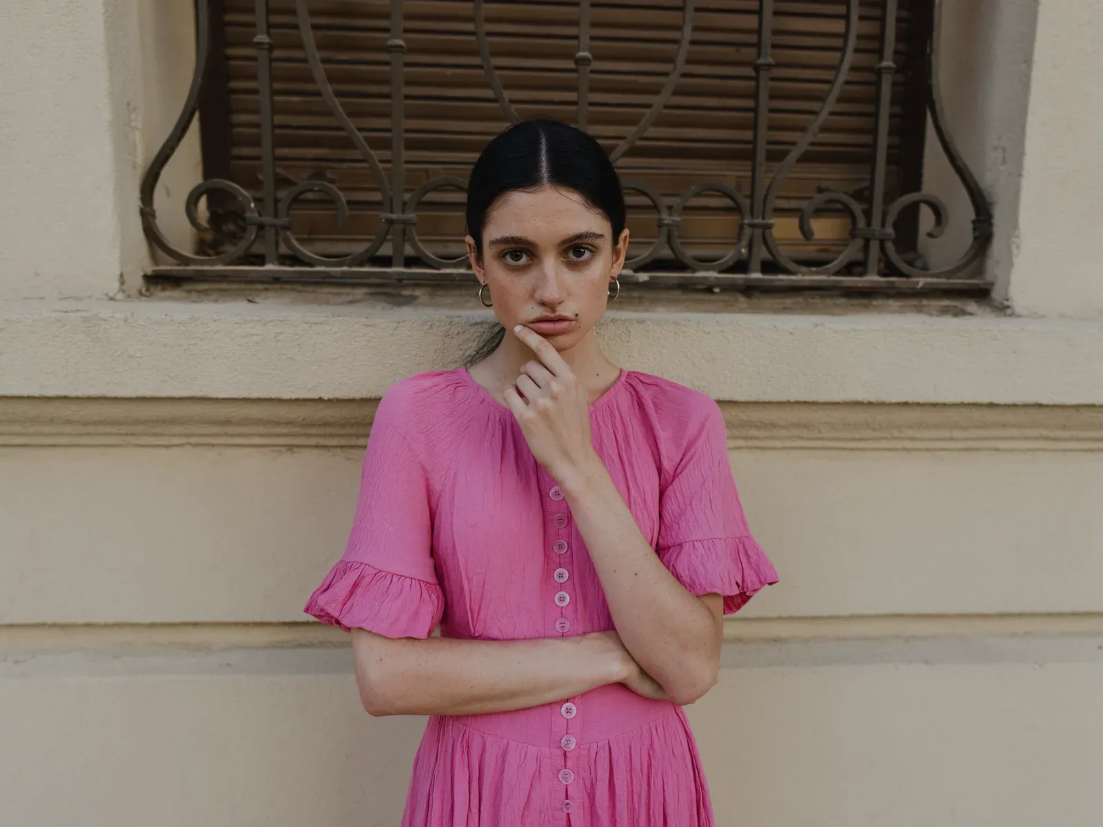 A woman in a pink dress against a cream wall