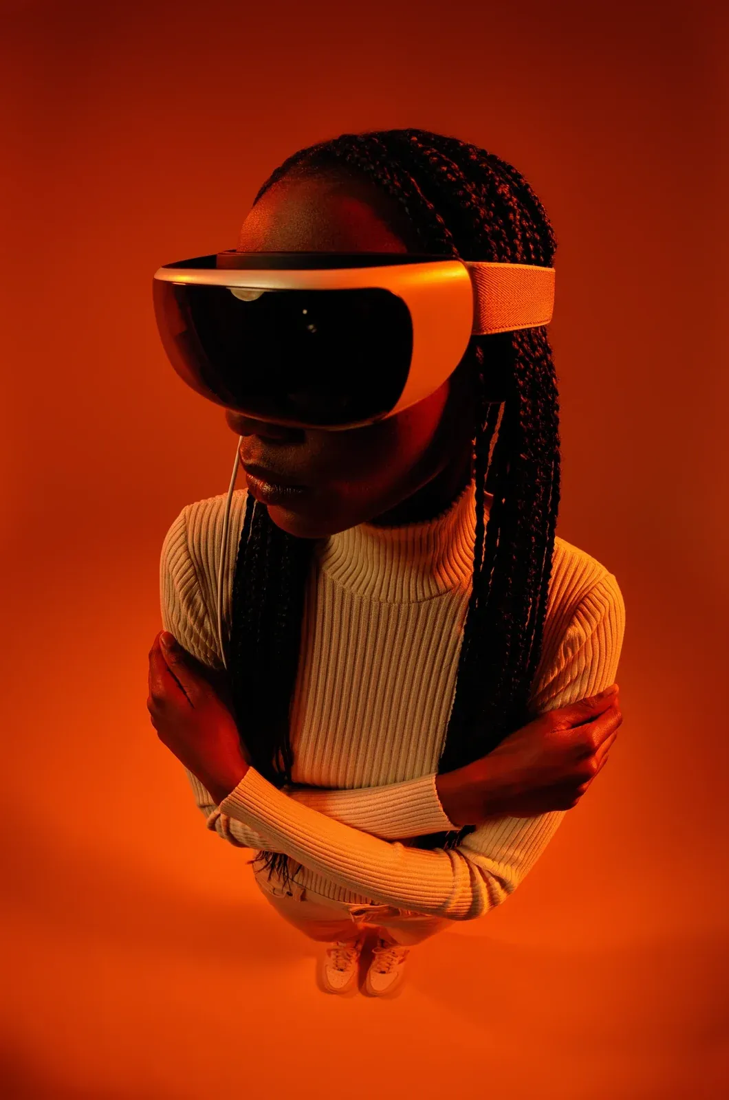 A woman with long braids in a white headset, arms crossed, seen from above in orange light.
