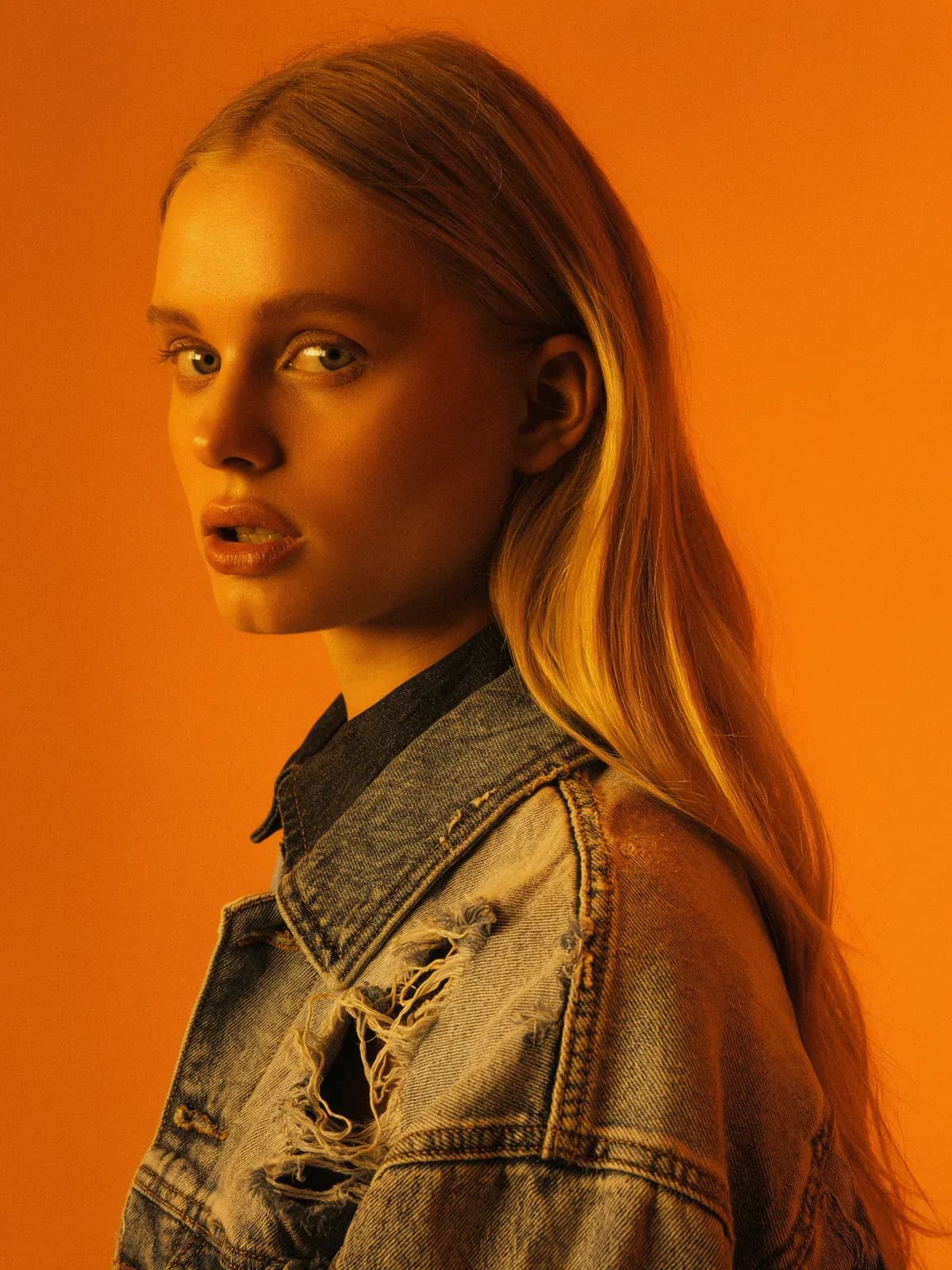 Portrait of a woman in a denim jacket against orange